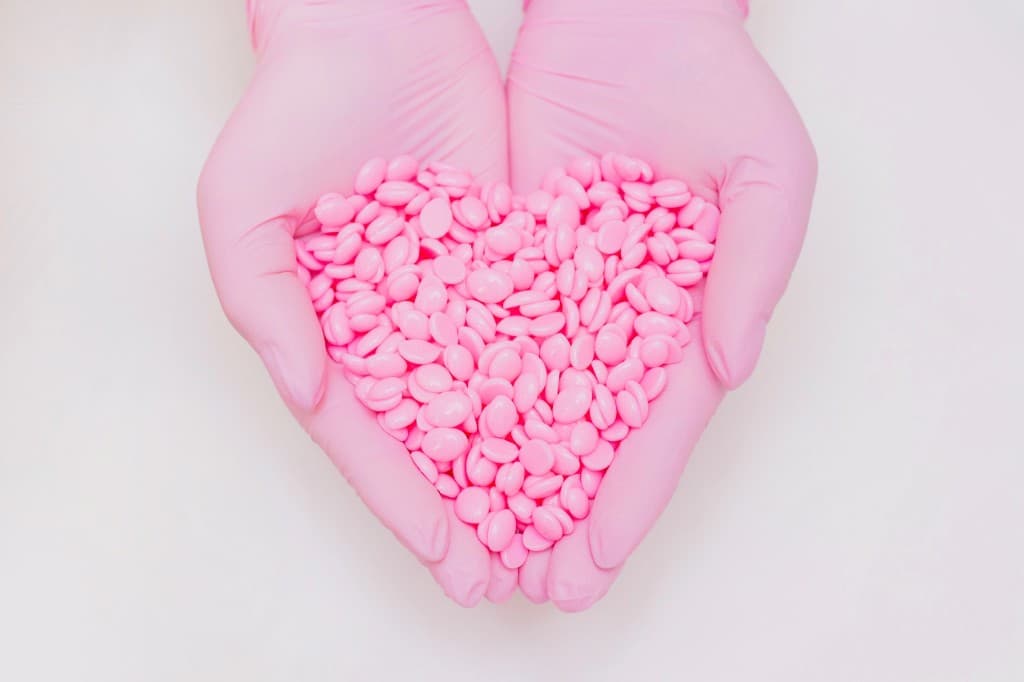 Pink wax beads held in the shape of a heart by gloved hands at Alexandria Smooth Wax & Beauty